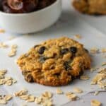 Oatmeal Tahini Cookies on a white paper with chocolate chips with dates in the background