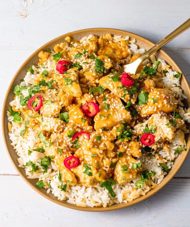 orange glazed tofu served over white rice, topped with sesame seeds, chopped cilantro, and sliced red chili peppers