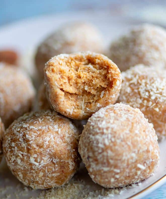 Close-up of healthy bounty bites coated in shredded coconut, with one bite taken to reveal a soft, creamy coconut-almond center.