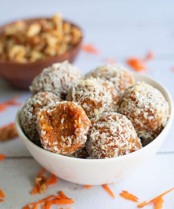 A white bowl with carrot-cake-bliss-balls and walnuts in the background