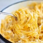 Creamy light high-protein pasta twirled on a fork, coated in a rich cheesy sauce and served in a bowl with herbs and shredded cheese on top.
