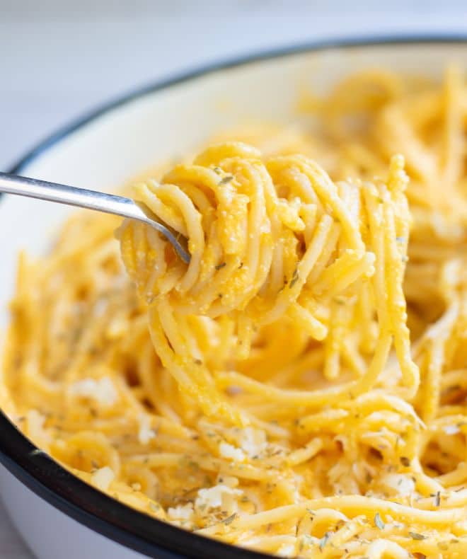 Creamy light high-protein pasta twirled on a fork, coated in a rich cheesy sauce and served in a bowl with herbs and shredded cheese on top.