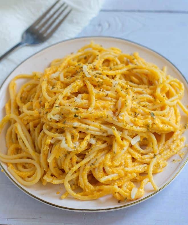 Plate of light creamy high-protein pasta with a rich cheesy sauce, topped with herbs and shredded cheese, served fresh with a fork twirling the noodles.