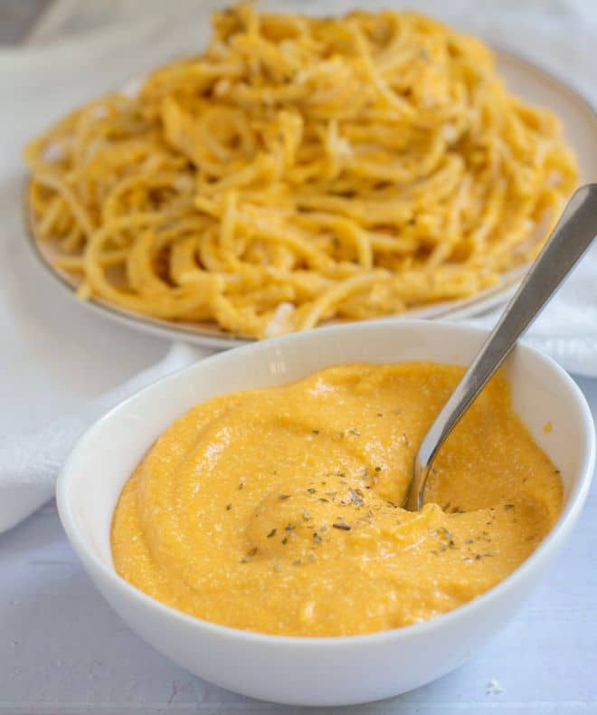 Plate of light creamy high-protein pasta in the background with a rich cheesy sauce in the front in a white bowl
