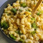 A bowl of high protein creamy mac and cheese with broccoli with a wooden spoon in the middle