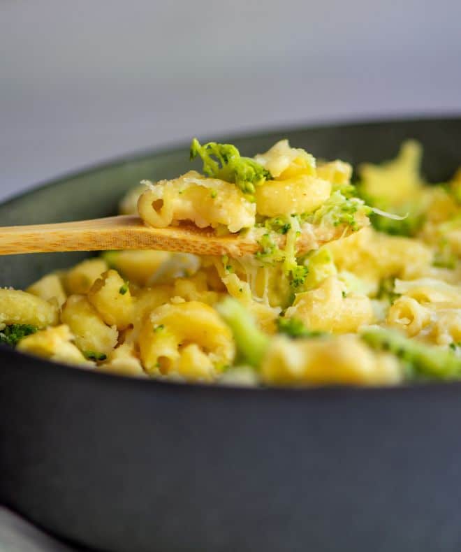 A spoon with creamy light mac and cheese made with elbow macaroni and broccoli florets, topped with grated Parmesan cheese.