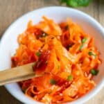 A white bowl filled with carrot ribbon salad, with chopsticks picking up a piece