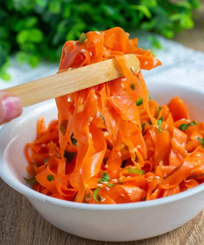 A white bowl filled with carrot ribbon salad, with chopsticks picking up a piece