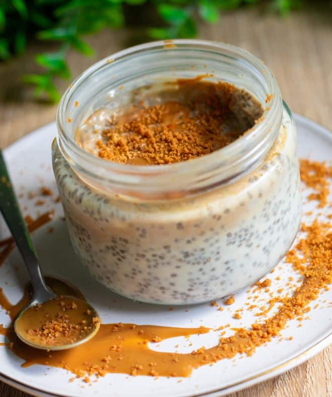 High-Protein Biscoff Chia Pudding in a jar on a white plate with a spoon on the side