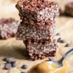 Three Chocolate Peanut Butter Crispy Bars stacked on top of each other, with a spoonful of peanut butter beside them