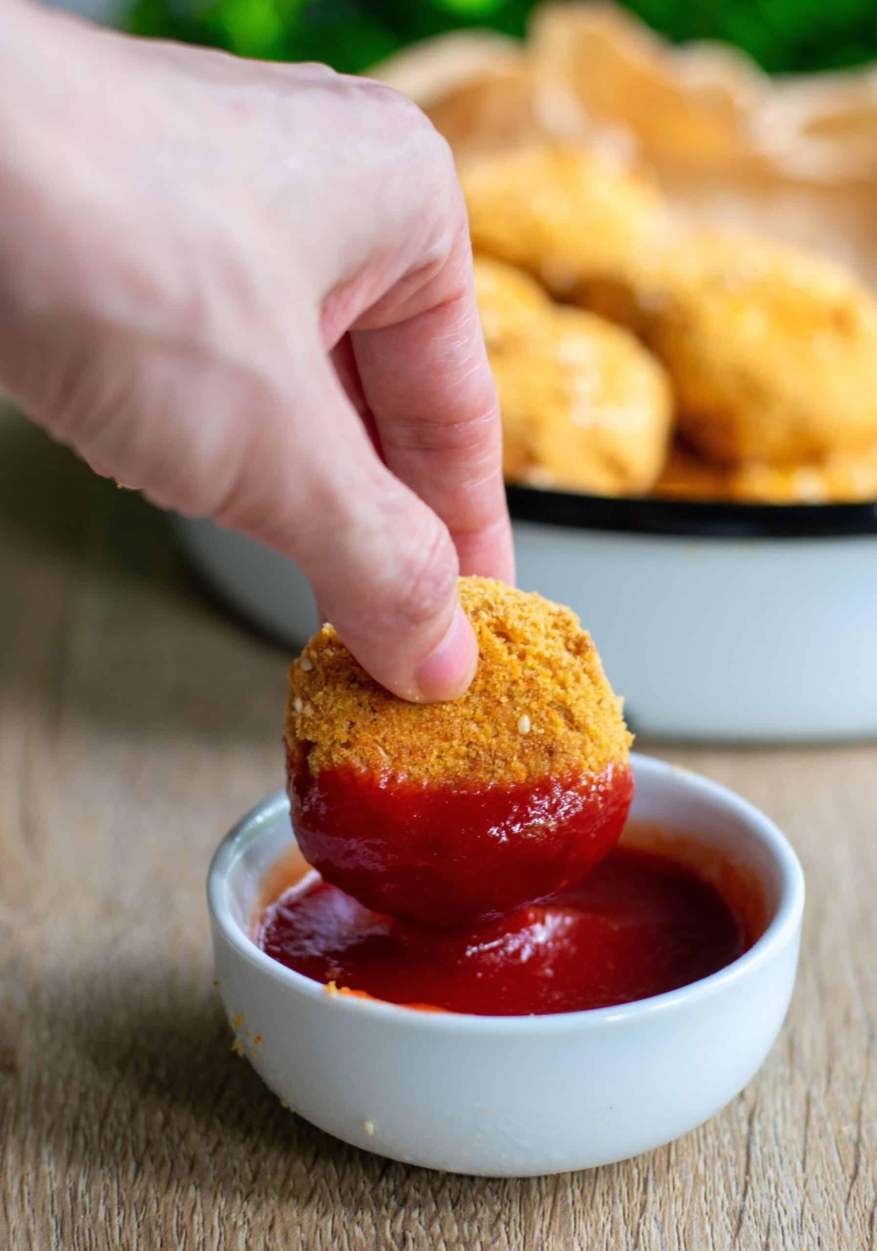 A hand dipping a Crispy Tofu Baked Nugget in a bowl of ketchup